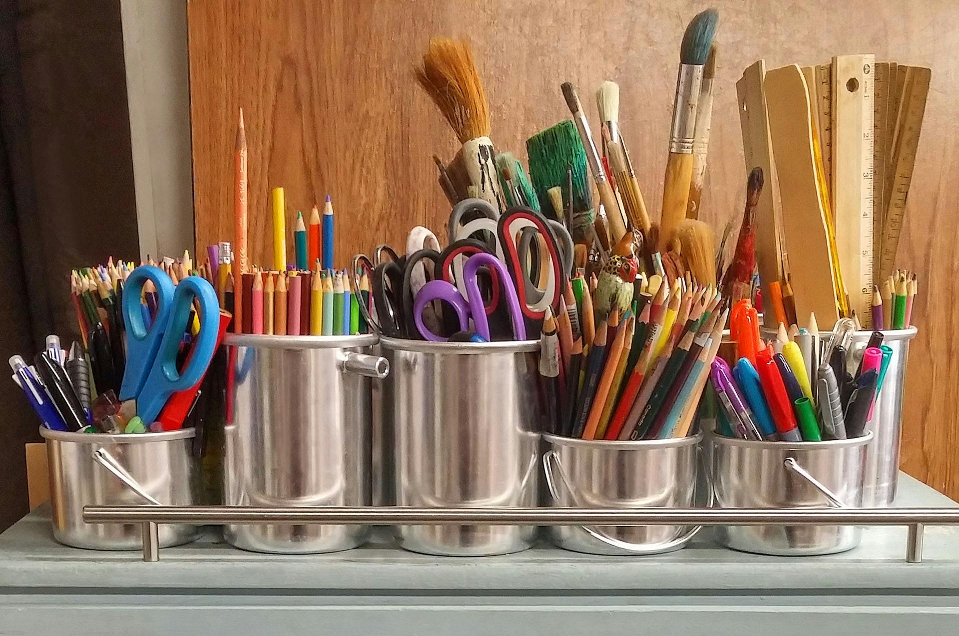 A diverse collection of art supplies in metallic buckets on a wooden table.