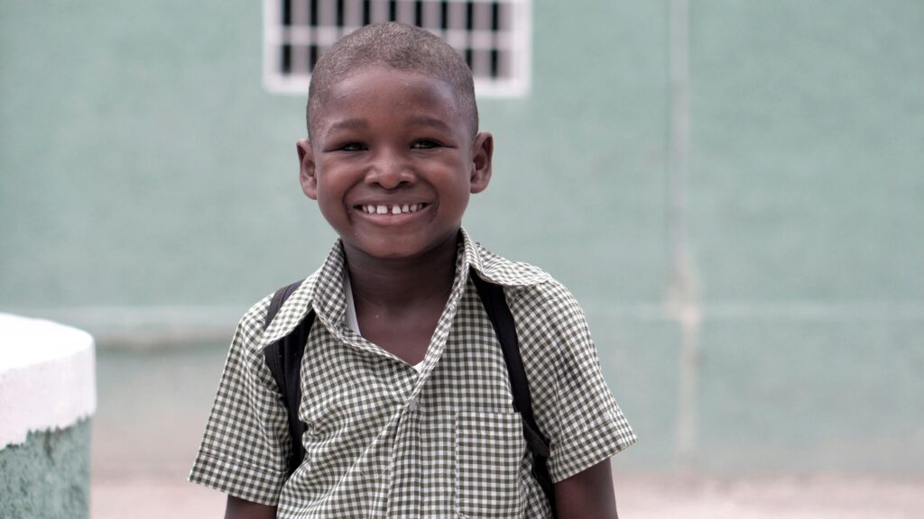 A cheerful Haitian boy smiling in his school uniform, showcasing innocence and happiness outdoors.